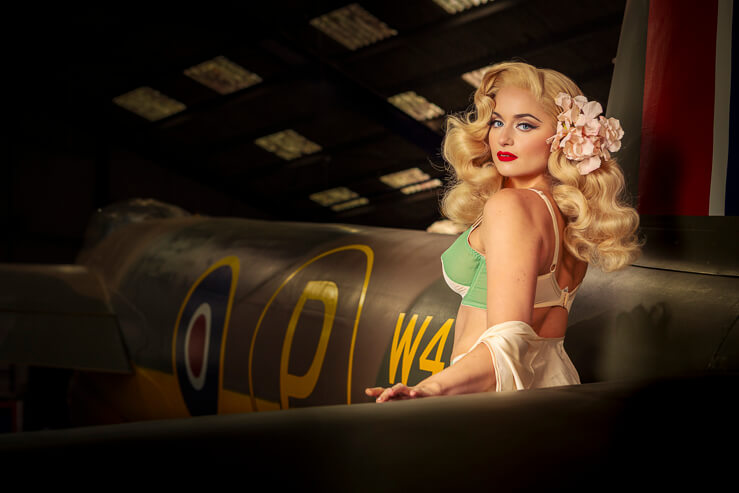 Did Derrier, a burlesque artist, poses for a photograph beside a warplane in an aircraft hanger.