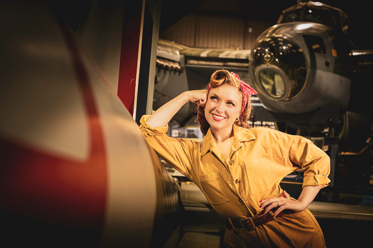 Felicity Furore, burlesque artist, poses for a photograph beside a warplane in an aircraft hanger.