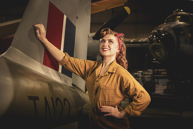 Felicity Furore, burlesque artist, poses for a photograph beside a warplane in an aircraft hanger.