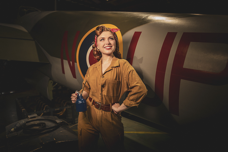 Felicity Furore, burlesque artist, poses for a photograph beside a warplane in an aircraft hanger.