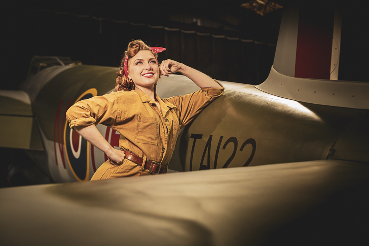 Felicity Furore, burlesque artist, poses for a photograph beside a warplane in an aircraft hanger.