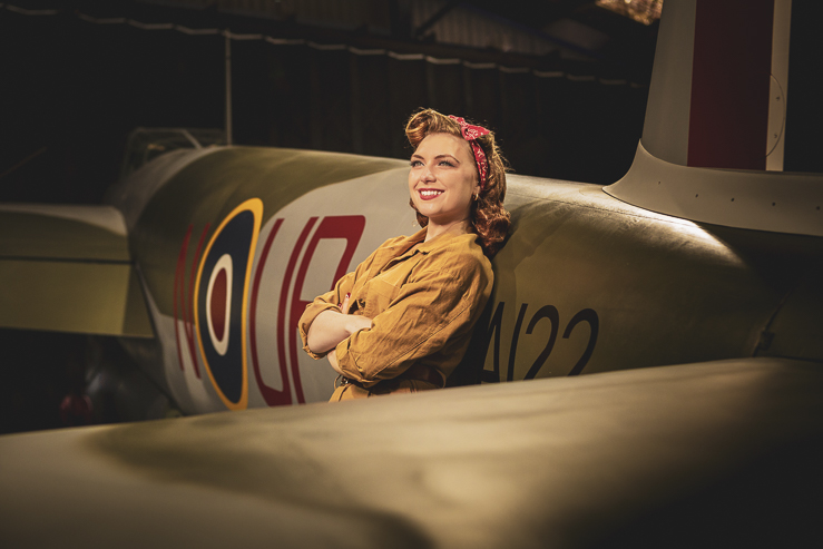 Felicity Furore, burlesque artist, poses for a photograph beside a warplane in an aircraft hanger.