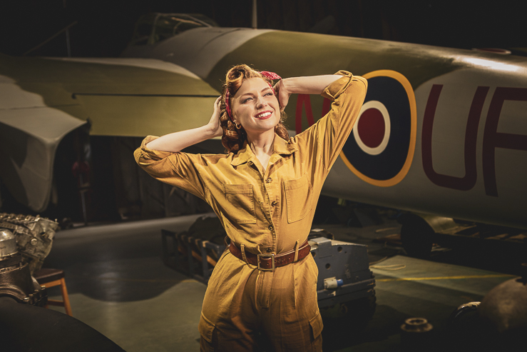 Felicity Furore, burlesque artist, poses for a photograph beside a warplane in an aircraft hanger.