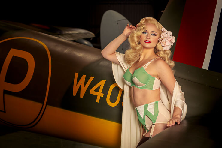 Did Derrier, a burlesque artist, poses for a photograph beside a warplane in an aircraft hanger.
